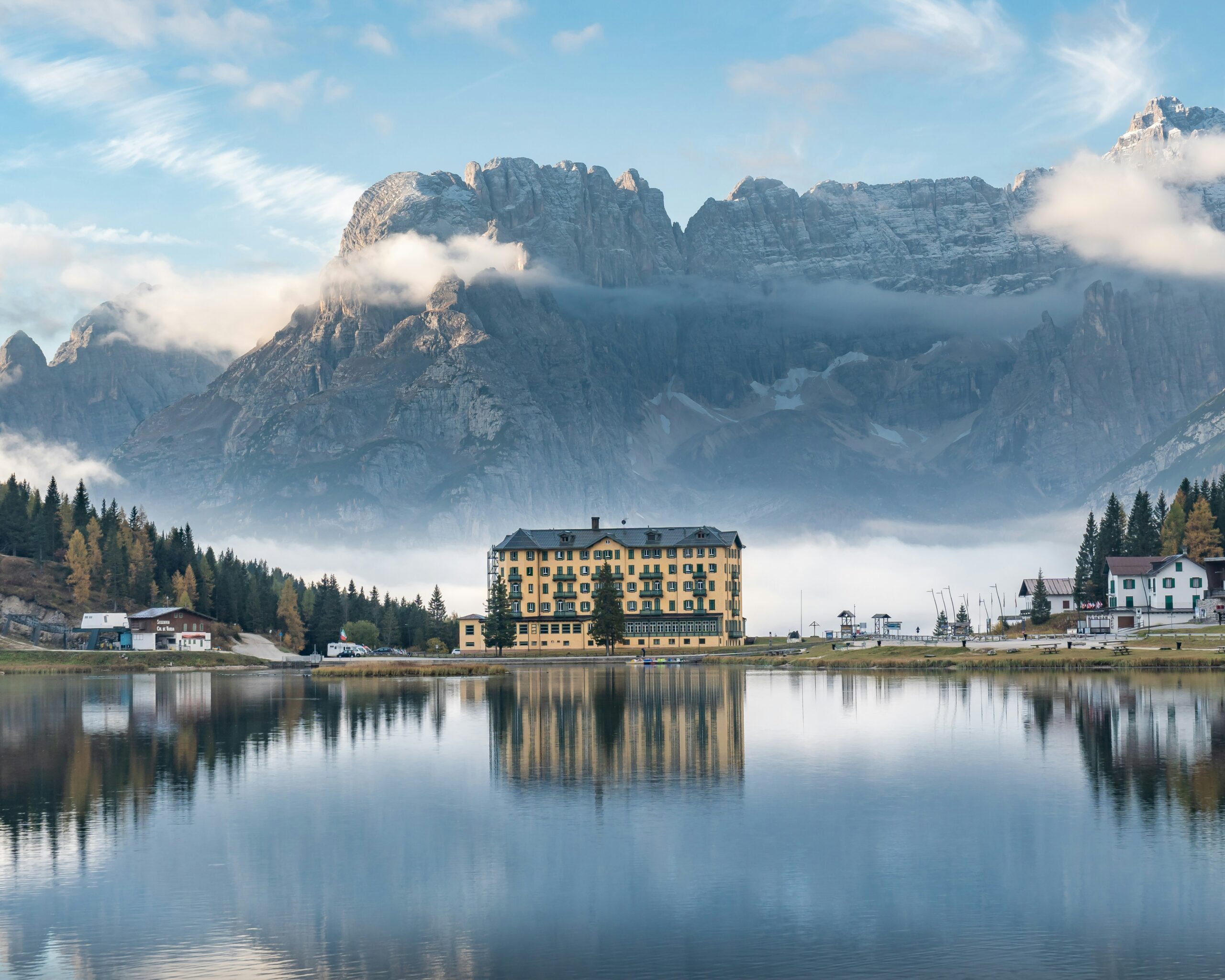 A luxury bus parked beside a picturesque lake surrounded by mountains.
