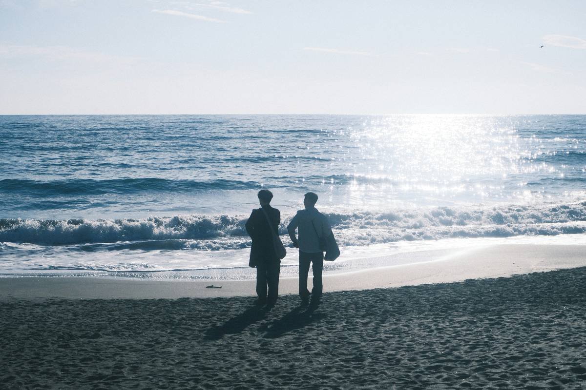 Two people stand on a beach facing the ocean